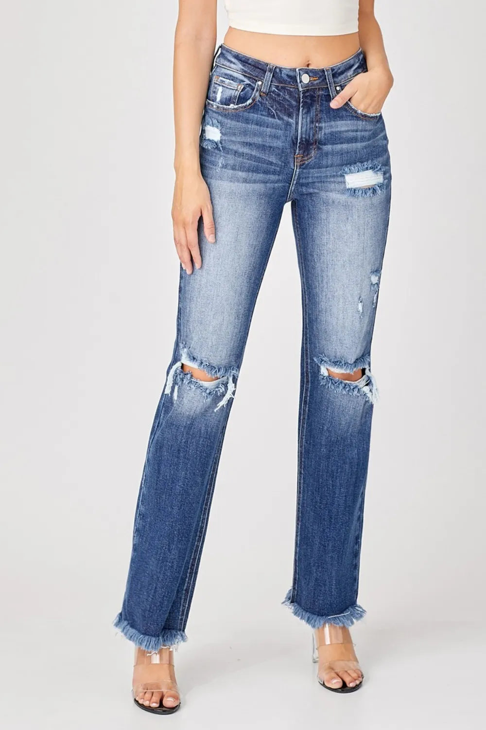 Distressed blue jeans worn by a person on a white background
