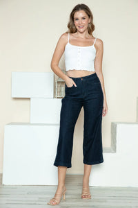 Woman wearing a white top and dark blue jeans standing on white blocks against a light background