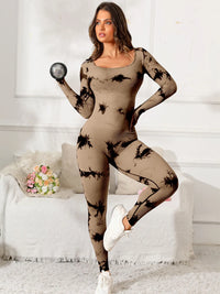Woman wearing a beige bodysuit with black patterns in a room with a white couch and flowers.