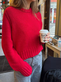Person wearing a red sweater holding a coffee cup in an urban setting.