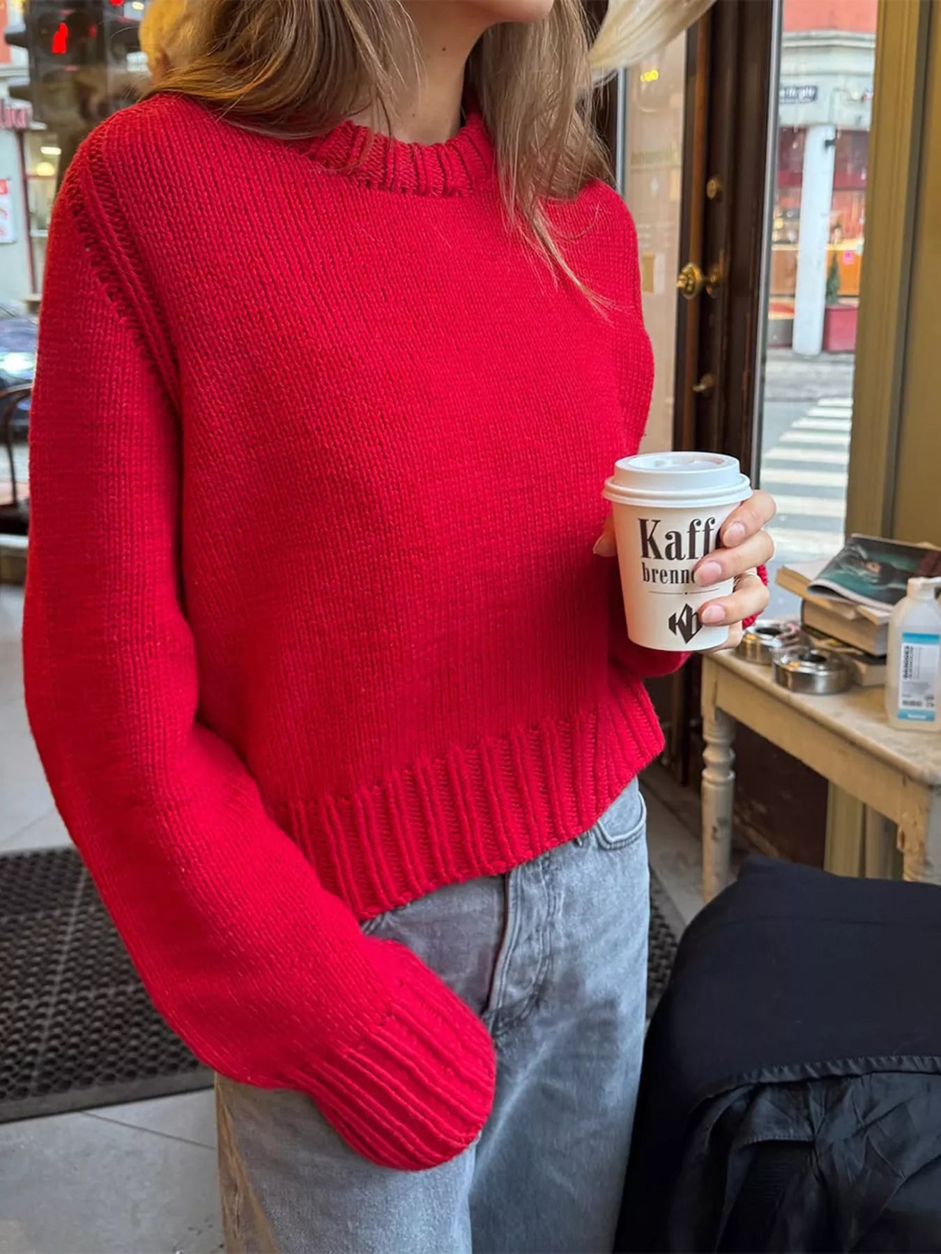 Person wearing a red sweater holding a coffee cup in an urban setting.