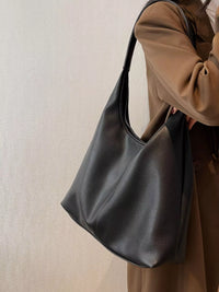 Person holding a black leather handbag against a neutral background