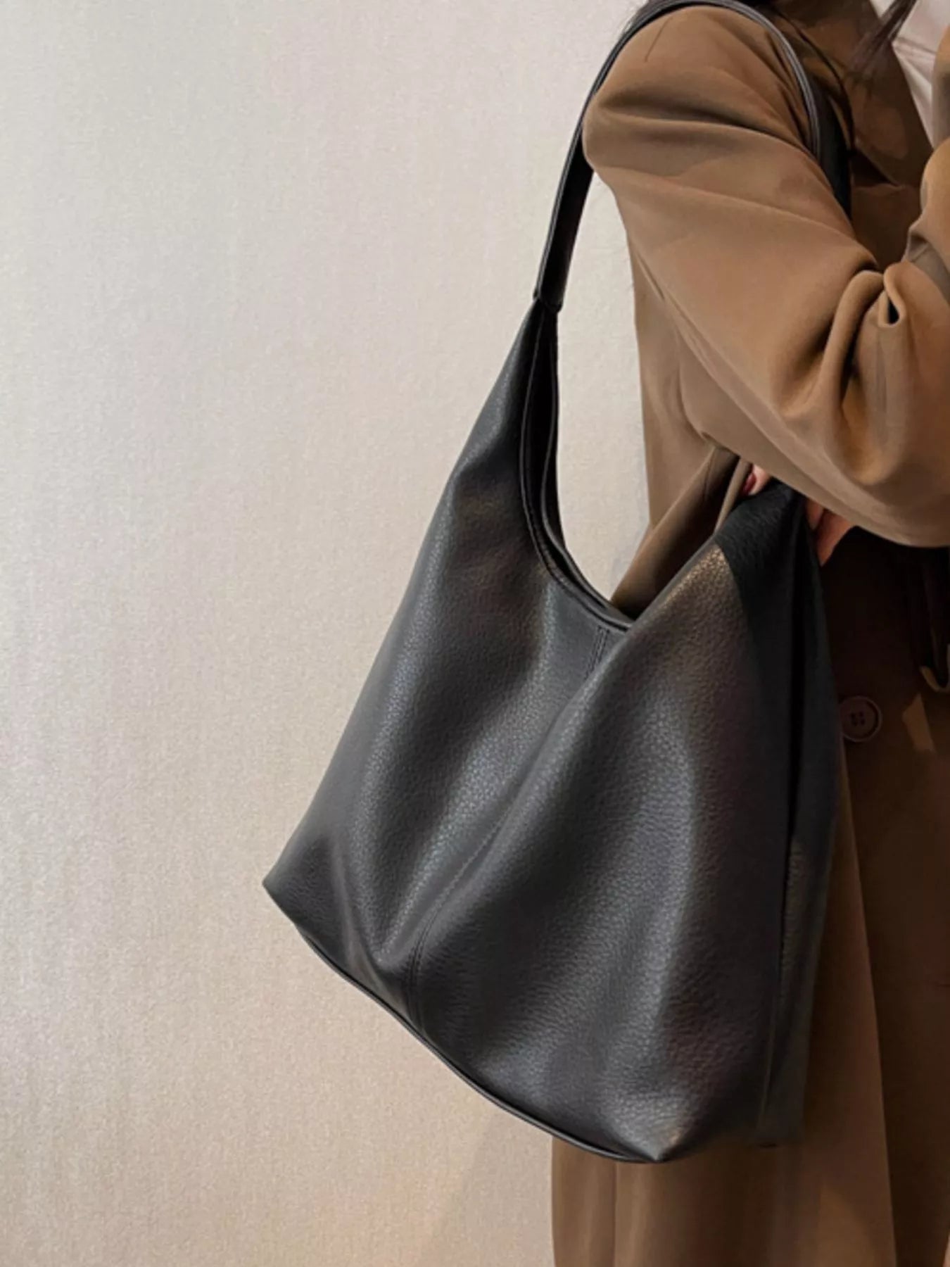 Person holding a black leather handbag against a neutral background