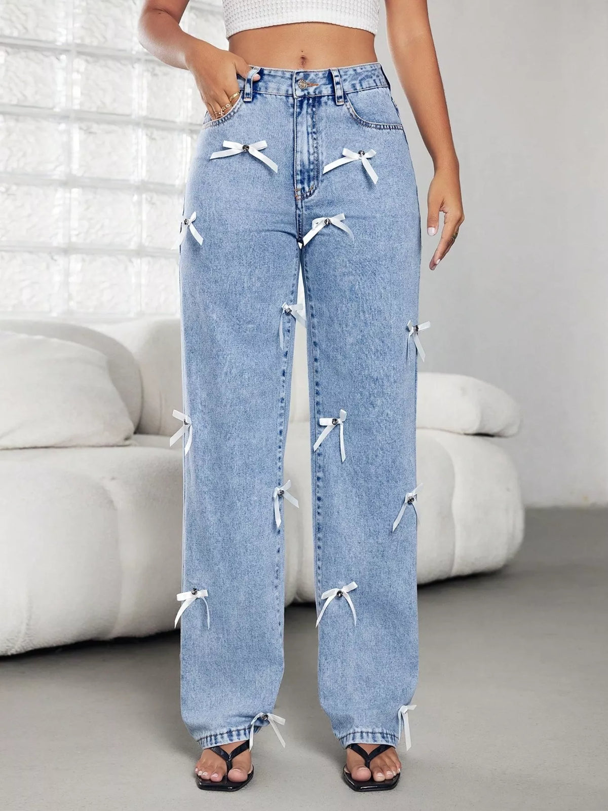 Light blue jeans with white bows worn by a person in a minimalistic room.