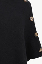 Close-up of a black knit garment sleeve with decorative metallic buttons along the edge, shown against a plain light background.