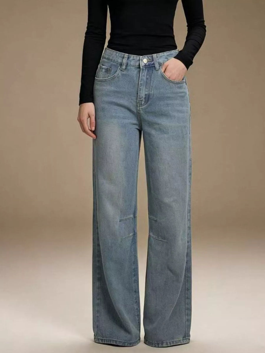 Person wearing blue jeans and a black top against a beige background