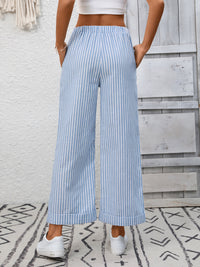 Person wearing blue and white striped wide-leg pants with a white top against a wooden panel background.