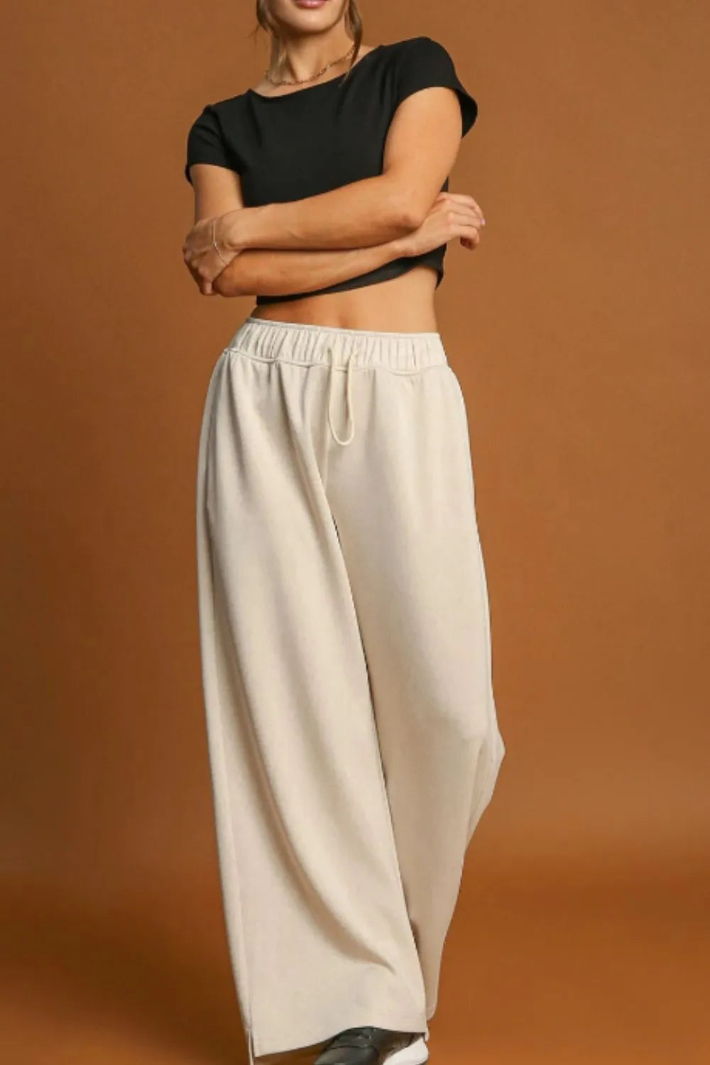 Person wearing a black top and beige wide-leg pants on a brown background