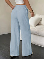 Person wearing light blue pleated pants in a room with a white couch.