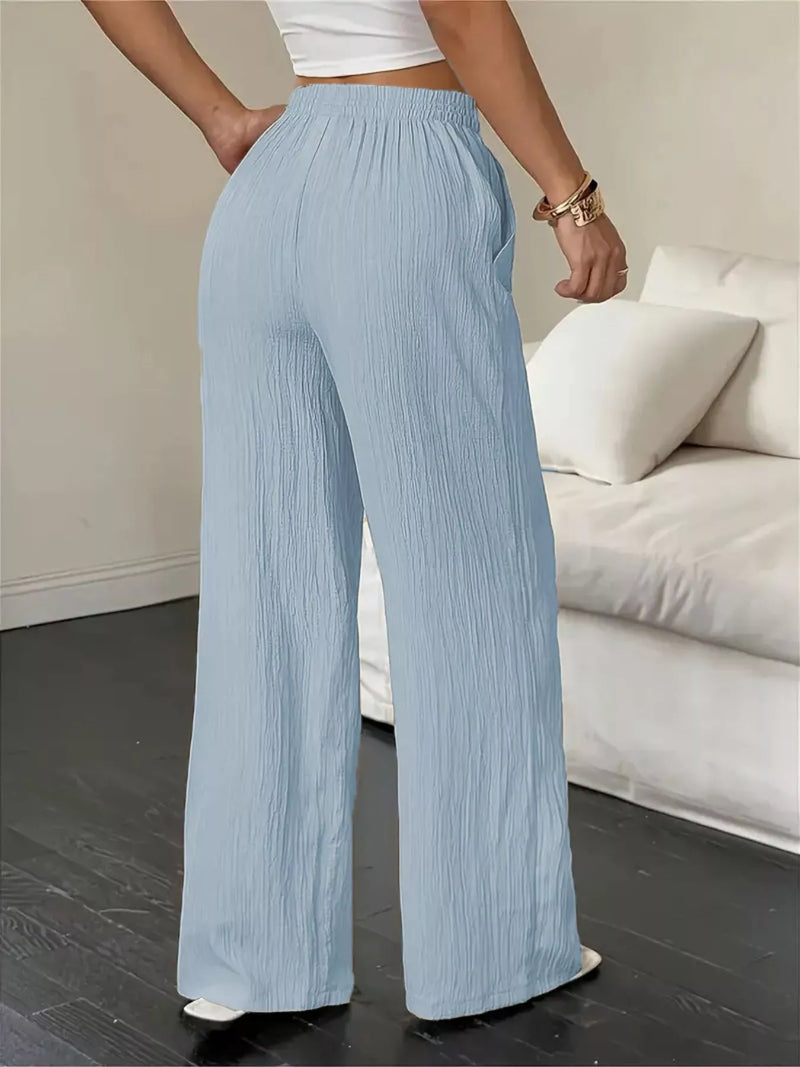 Person wearing light blue pleated pants in a room with a white couch.