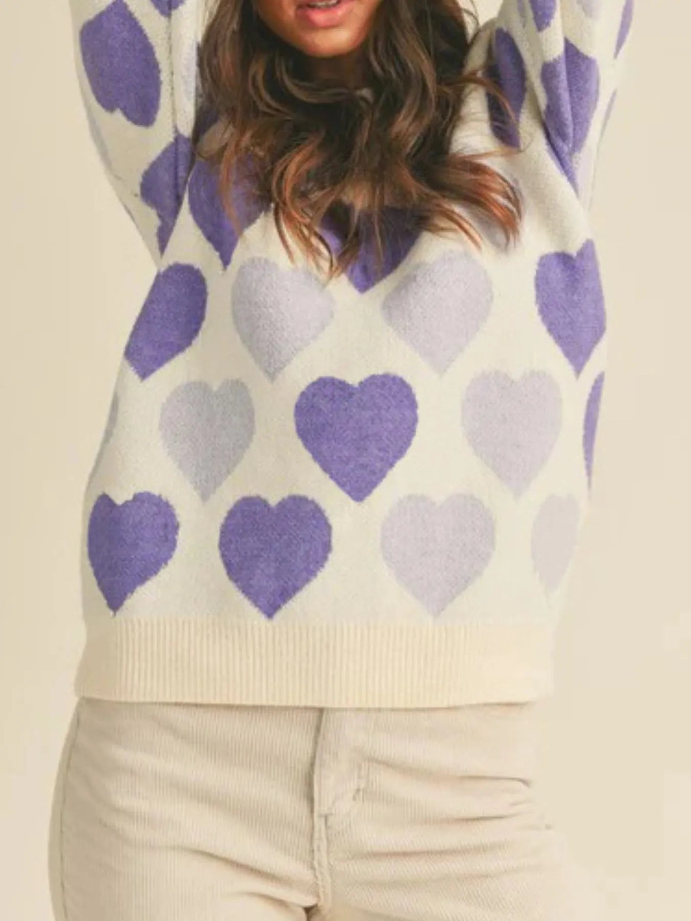 Person wearing a sweater with purple and light purple heart patterns on a beige background