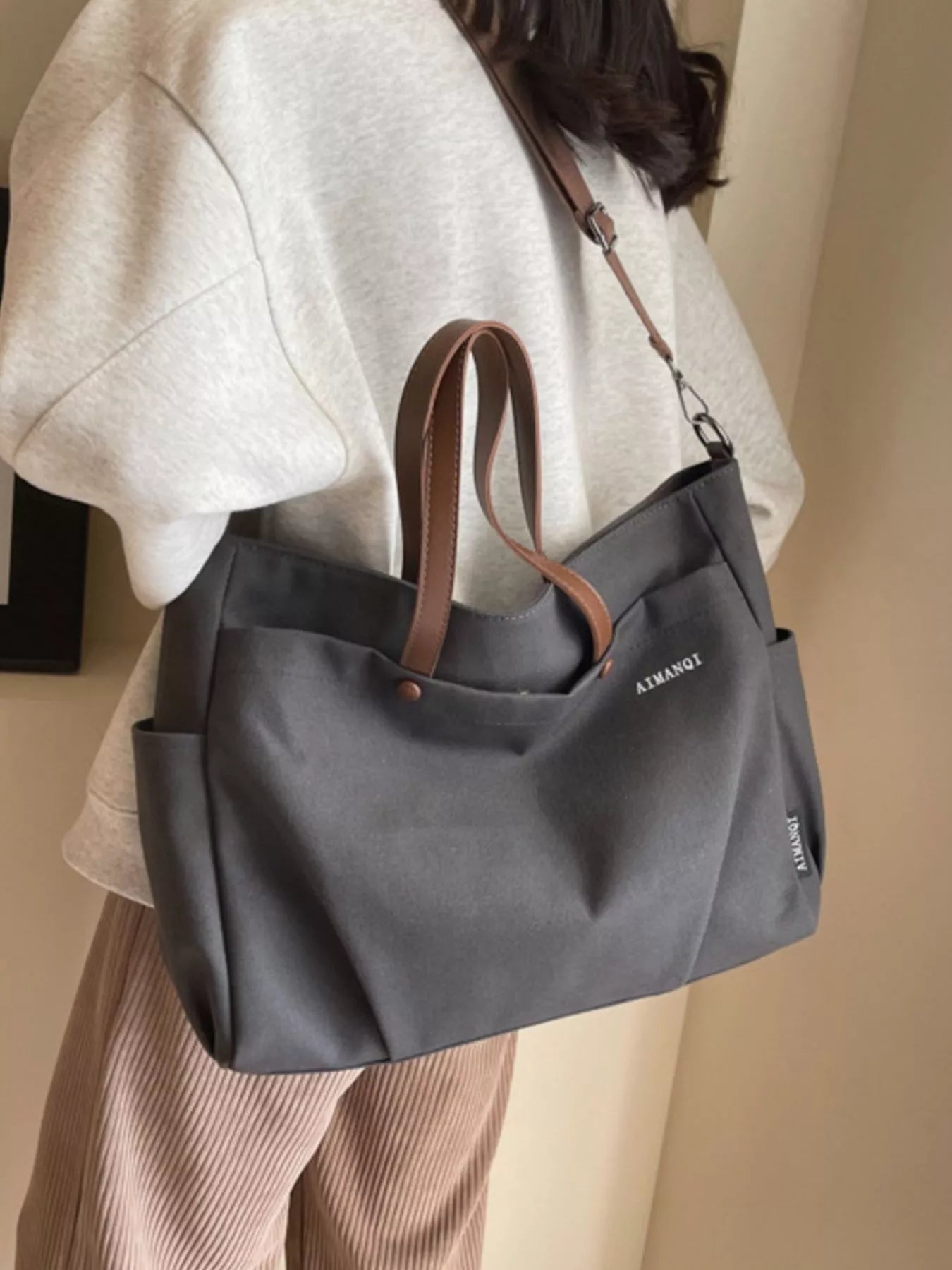 Person holding a gray handbag with brown straps against a neutral background