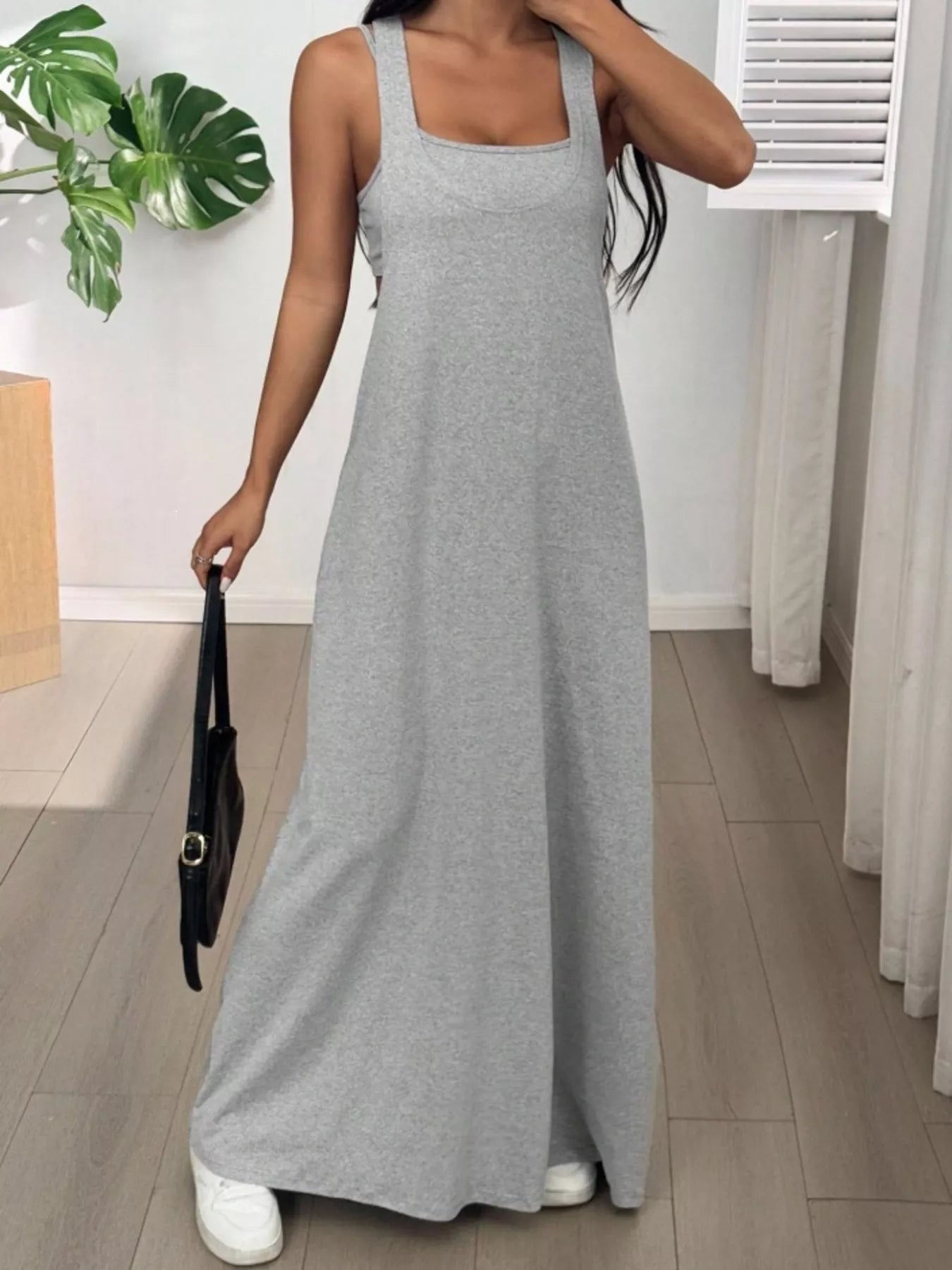 Woman wearing a gray dress holding a black handbag indoors.