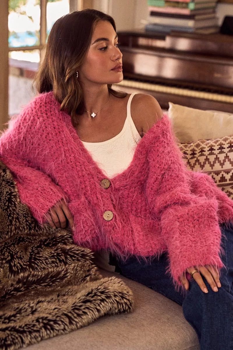 Woman wearing a pink cardigan with brown buttons sitting on a couch.