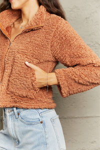 Person wearing a brown sherpa jacket with a neutral background
