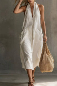 Woman wearing a white dress holding a woven bag against a neutral background
