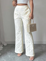 Person wearing white textured pants holding a wicker handbag against a plain background