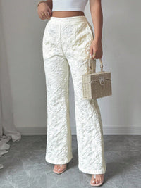 Person wearing white textured pants holding a wicker handbag against a plain background