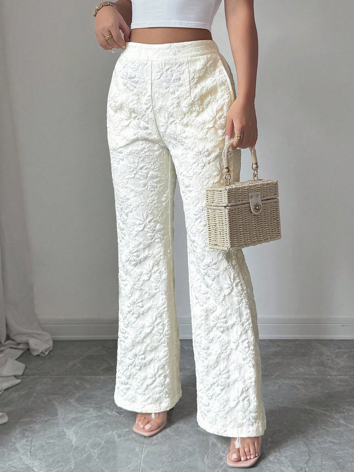 Person wearing white textured pants holding a wicker handbag against a plain background
