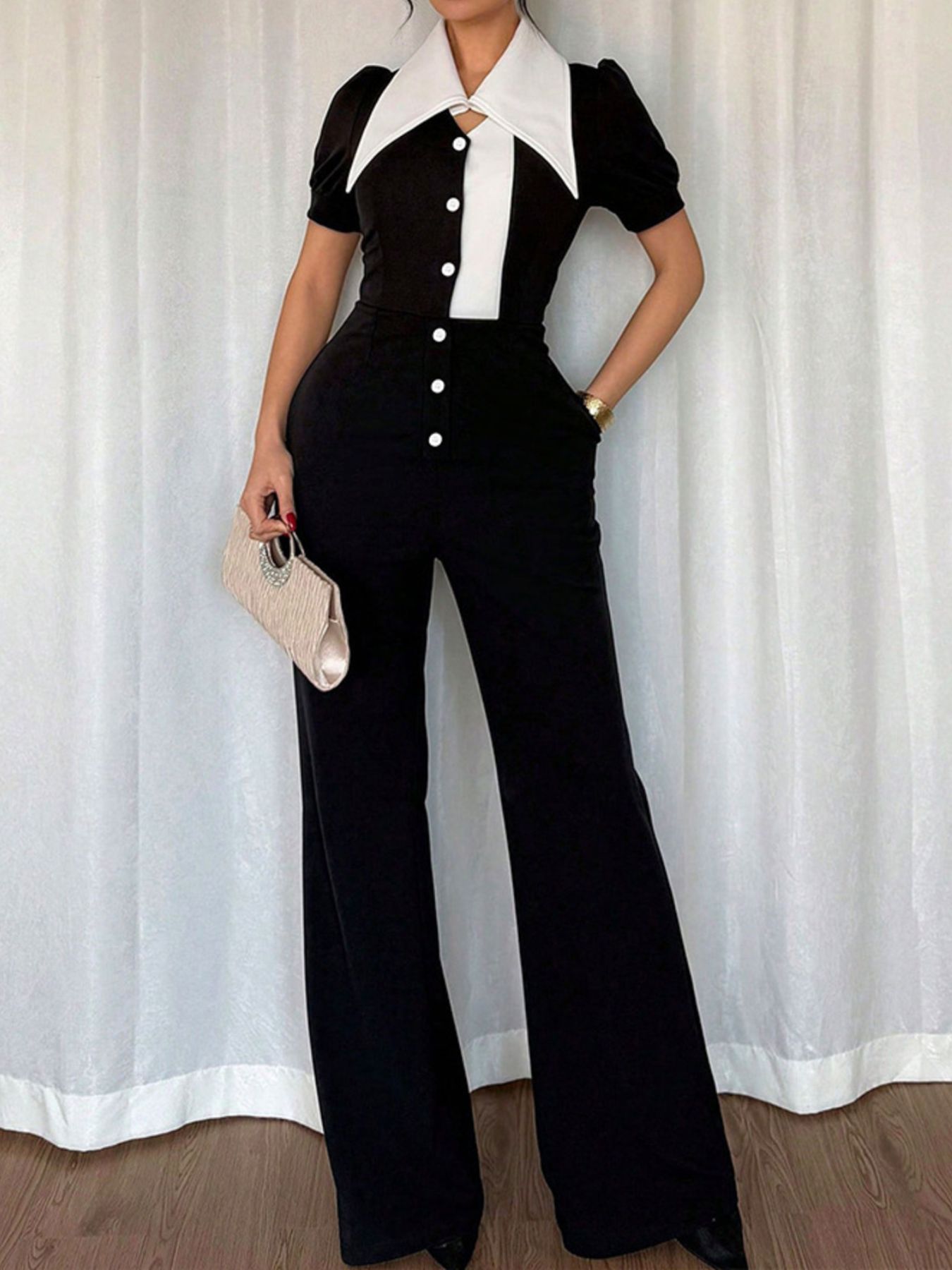 Person wearing a black and white outfit with a white curtain background