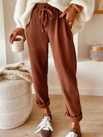 Person wearing brown ribbed pants and white sneakers, holding a ceramic cup indoors.