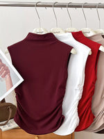 Three sleeveless tops in burgundy, white, and red hanging on a rack.