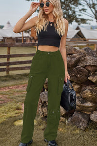 Woman wearing green cargo pants and a black top outdoors near a stone wall.