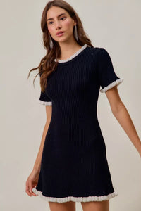 Woman wearing a navy ribbed dress with white trim on a plain background