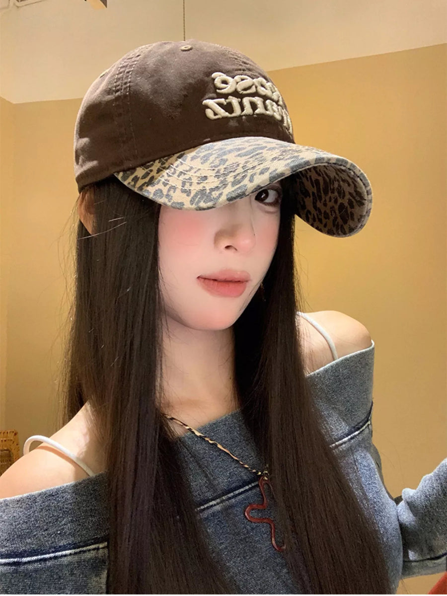 Person wearing a brown cap with leopard print visor against a beige wall.