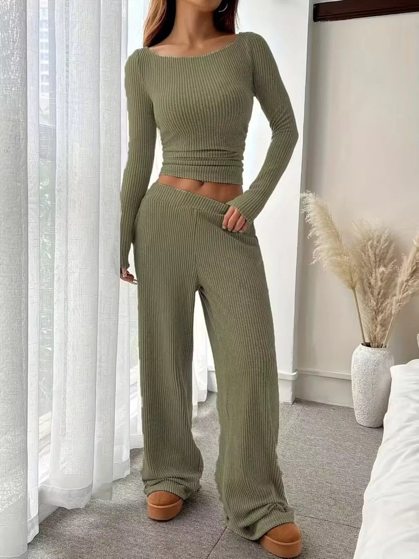 Person wearing a green ribbed knit outfit in a room with white curtains and a vase.