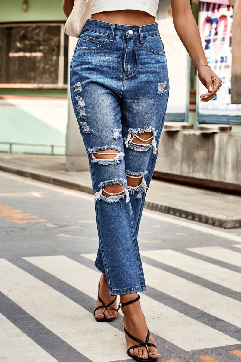 Person wearing ripped blue jeans on a city street.