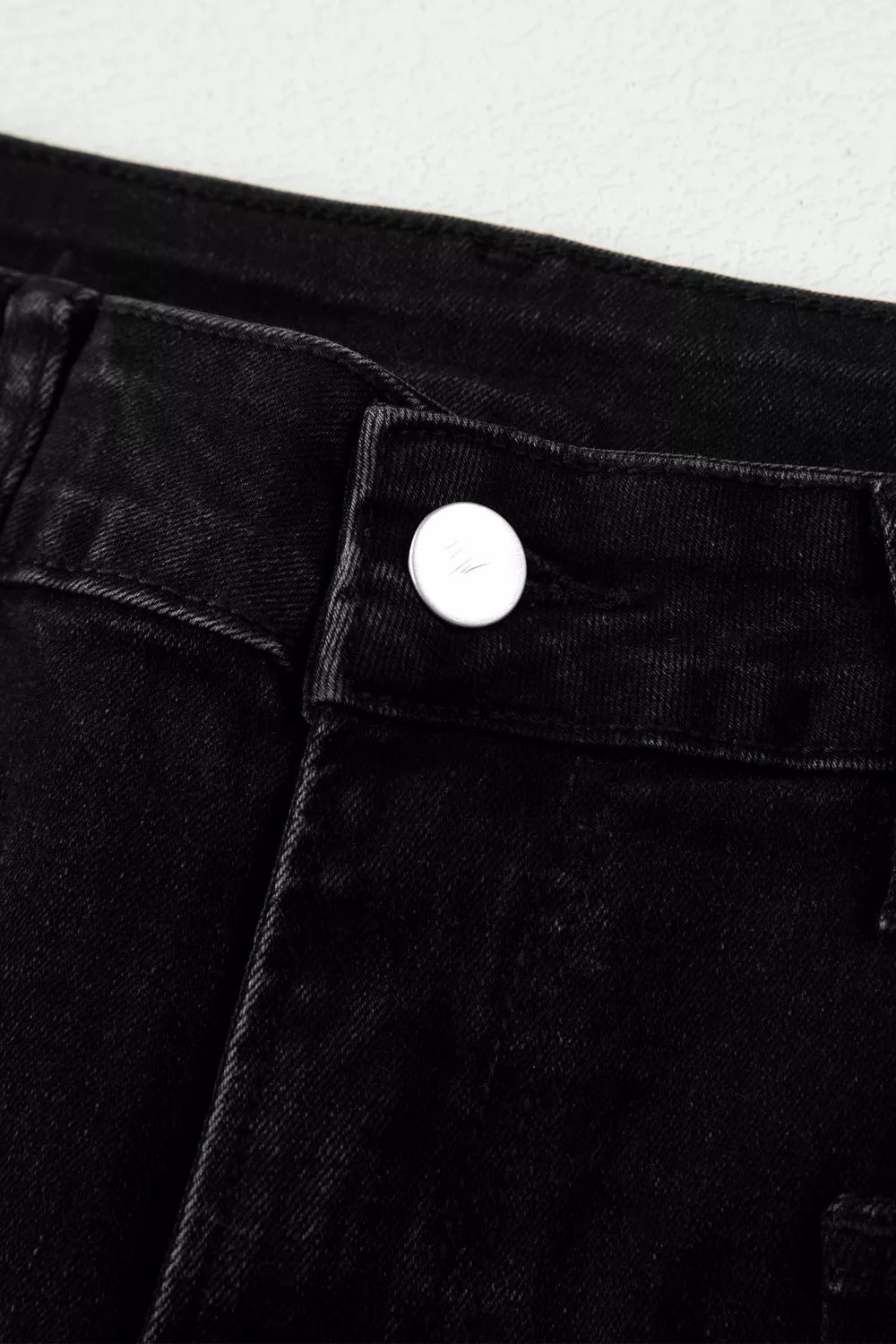 Close-up of a button on black pants against a white background