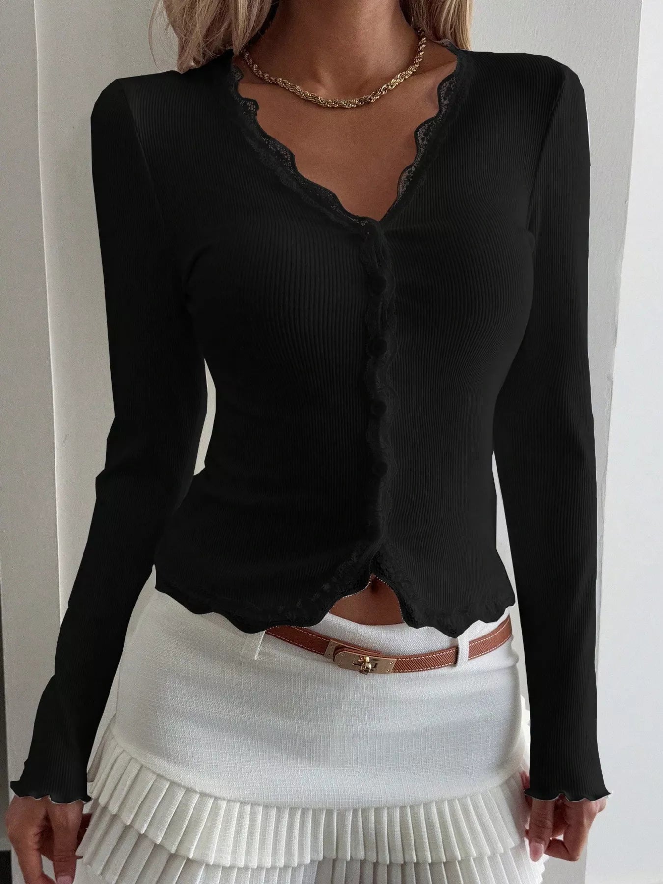 Black long-sleeve top with sheer neckline and white pleated skirt on a plain background
