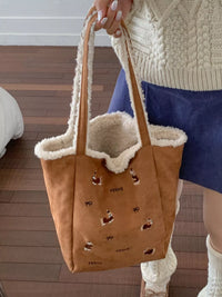Brown tote bag with animal prints held by a person wearing a white sweater and blue skirt.