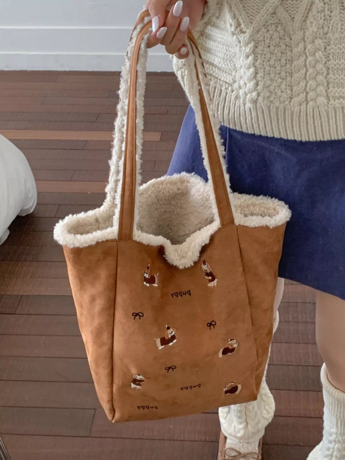 Brown tote bag with animal prints held by a person wearing a white sweater and blue skirt.