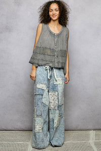 Woman wearing a sleeveless top and patchwork jeans against a gray background