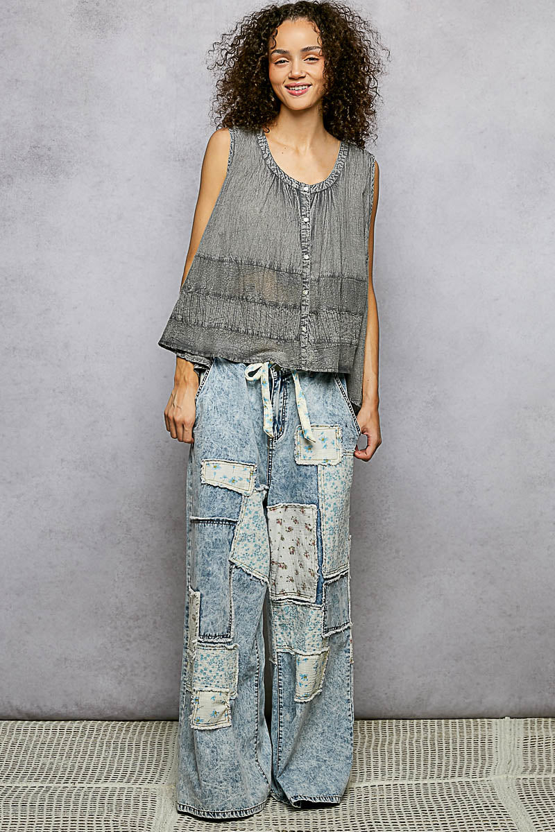 Woman wearing a sleeveless top and patchwork jeans against a gray background