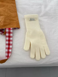 White glove on a textured white surface with a colorful fabric item in the background.