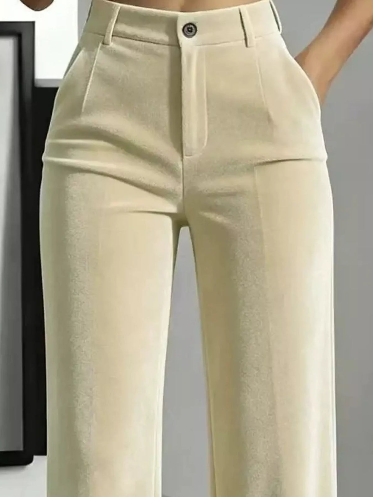 Close-up of a person wearing high-waisted light beige trousers with a structured waistband, front pleats, and a single visible button closure.