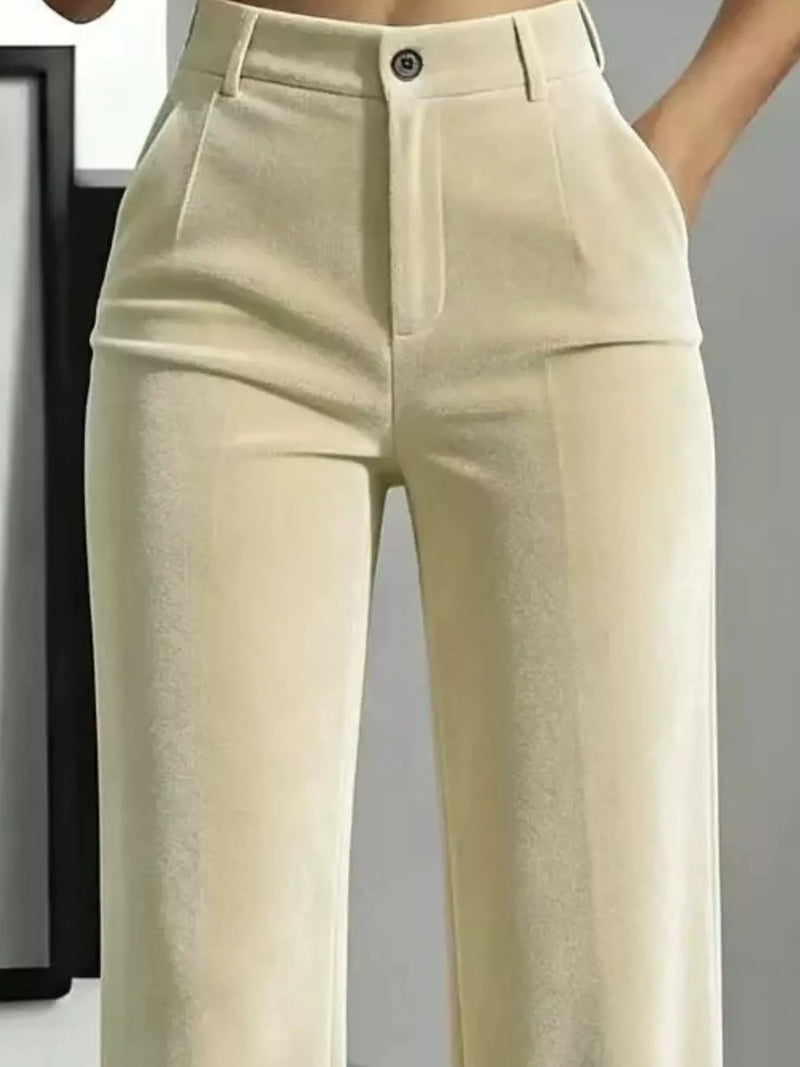 Close-up of a person wearing high-waisted light beige trousers with a structured waistband, front pleats, and a single visible button closure.