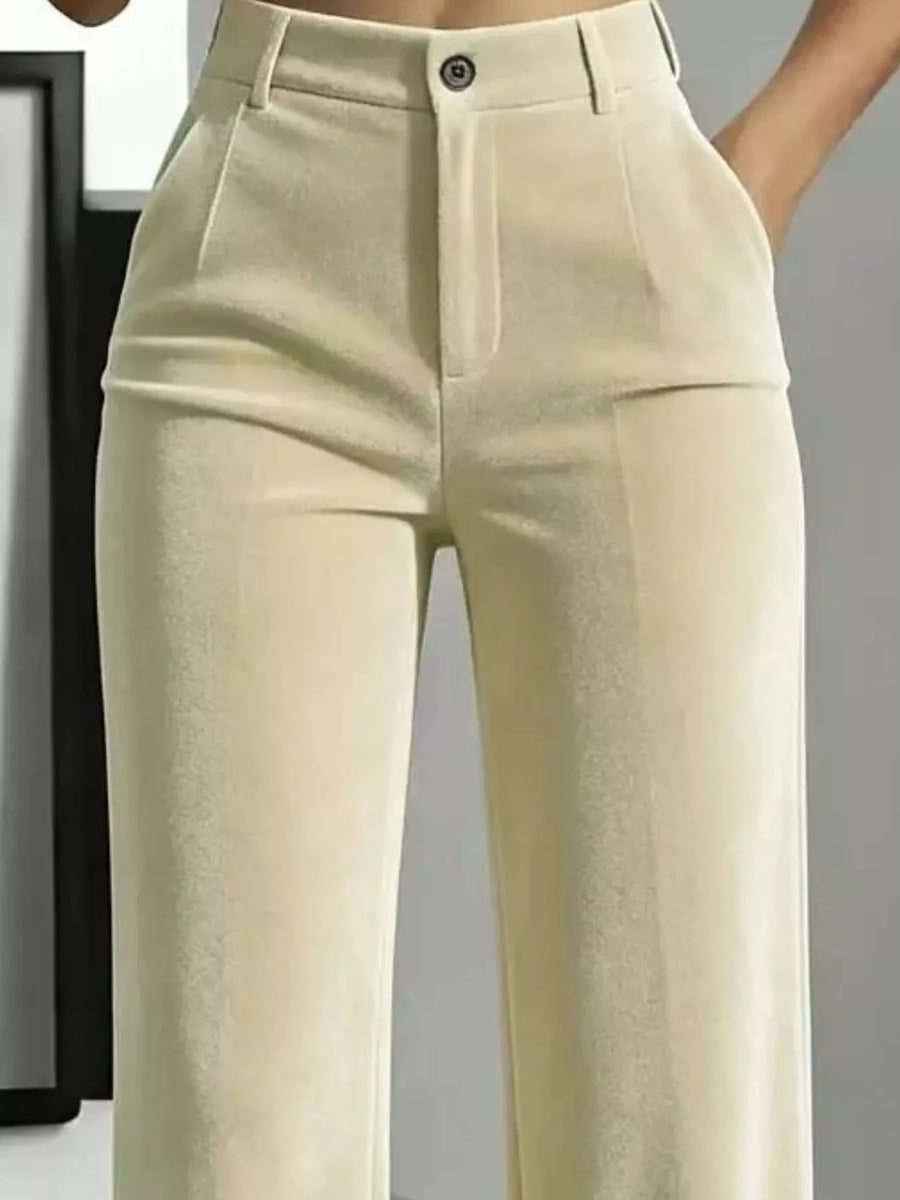 Close-up of a person wearing high-waisted light beige trousers with a structured waistband, front pleats, and a single visible button closure.