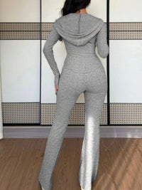 Person wearing a gray knit jumpsuit standing against a white wall with a geometric pattern.