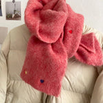 Person wearing a fluffy red scarf with heart decorations on a neutral background