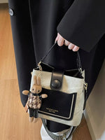 Person holding a black and beige handbag with a small plush toy attached, wearing a black coat.