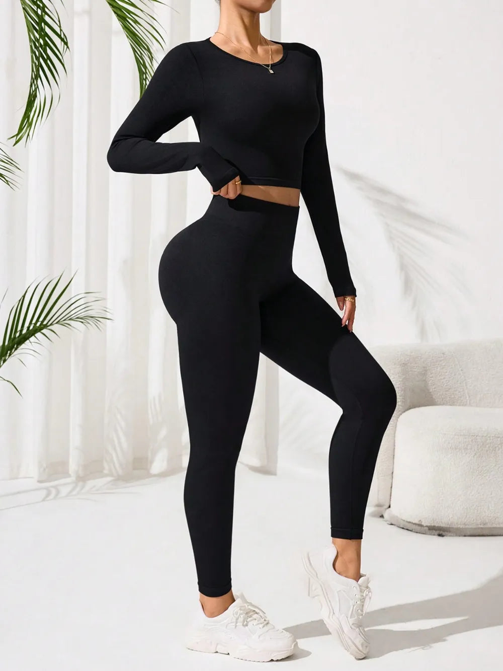 Person wearing a black athletic outfit in a minimalistic room with white curtains and a plant.