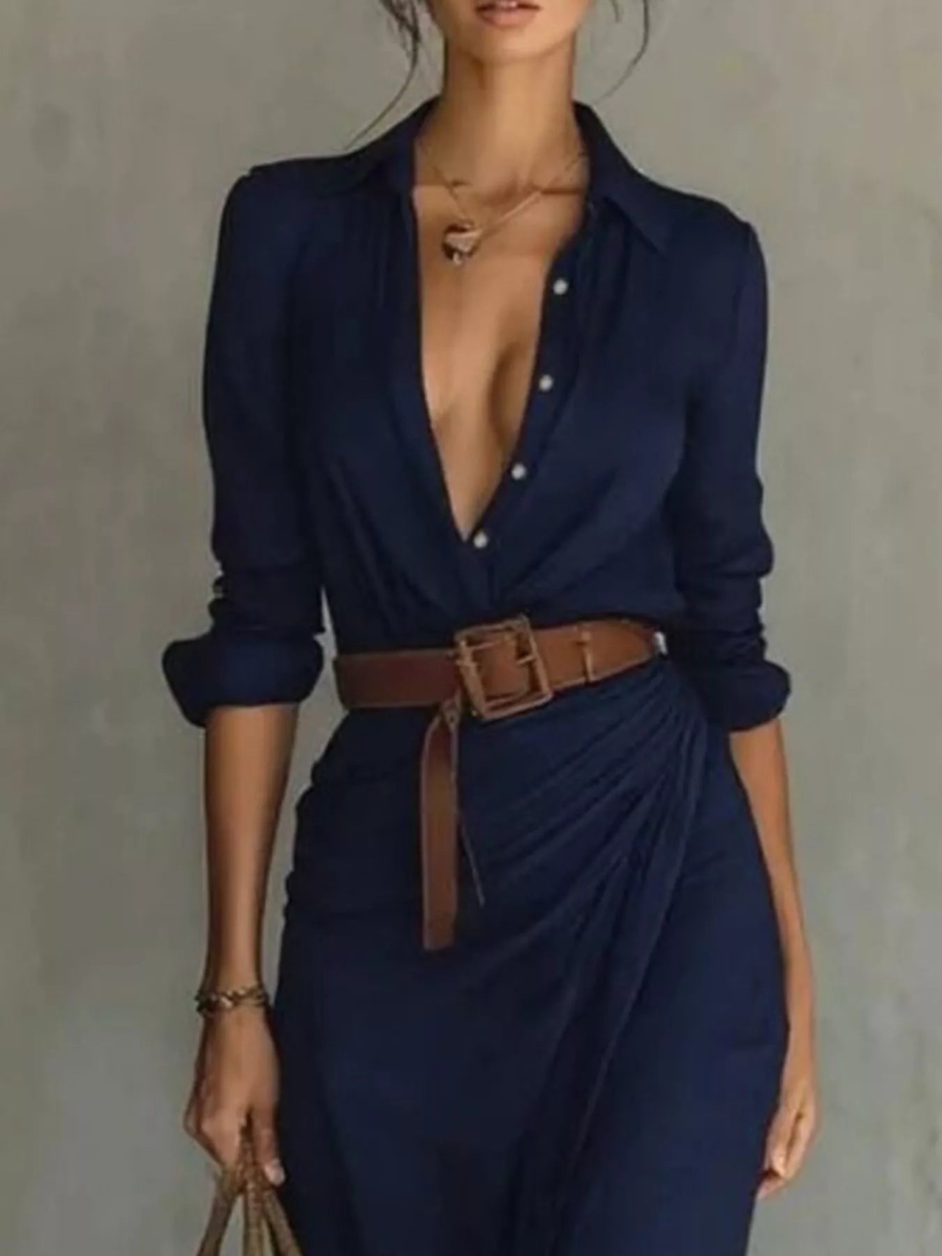 Woman wearing a navy blue outfit with a brown belt against a gray background