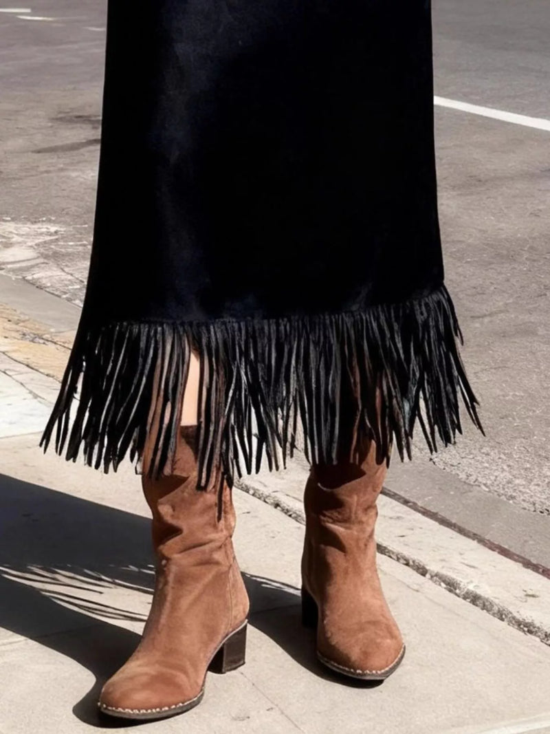 Brown suede boots with fringe on a black skirt against a street background