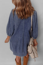 Person wearing a blue denim dress with brown boots and holding a beige handbag against a gray background