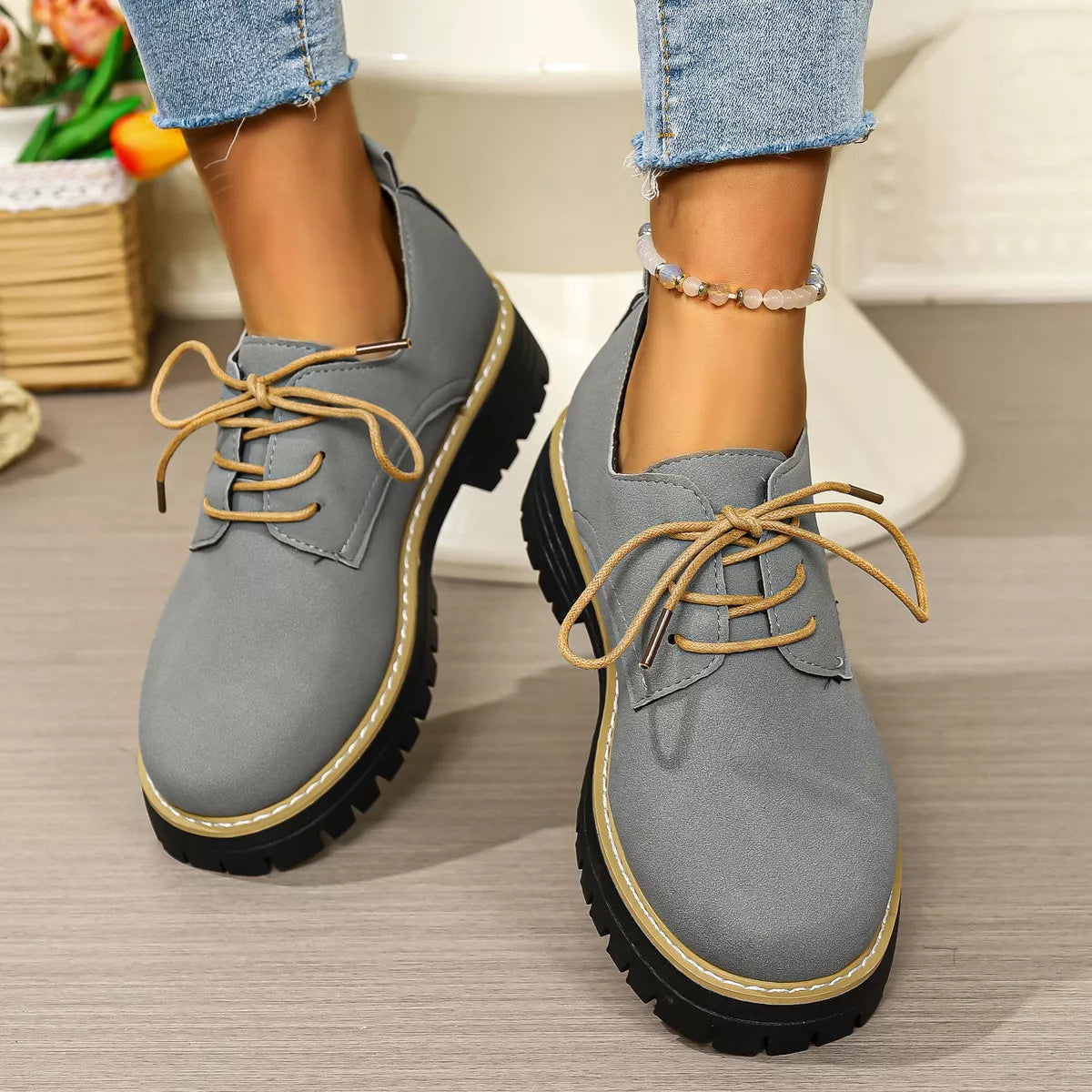Gray shoes with brown laces worn by a person on a wooden floor.