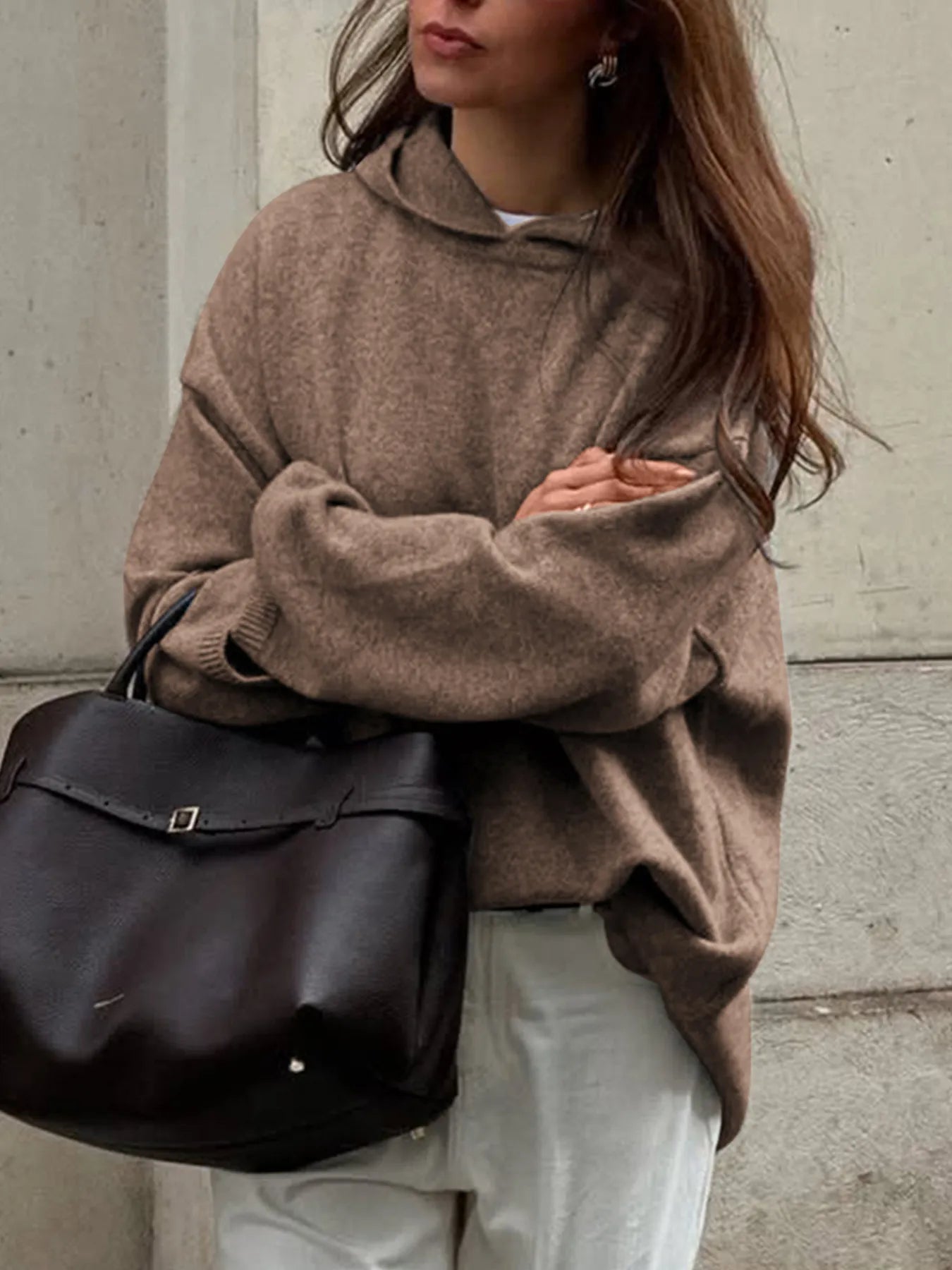 Person wearing a brown sweater holding a black bag against a neutral background